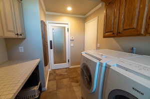 Laundry room with tile patterned flooring, washing machine and dryer, ornamental molding, and cabinets