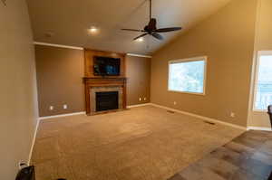 Unfurnished living room featuring a fireplace, carpet floors, ceiling fan, and a wealth of natural light