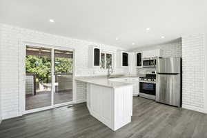 Kitchen featuring white cabinets, wood-type flooring, kitchen peninsula, and stainless steel appliances