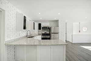 Kitchen featuring tasteful backsplash, light hardwood / wood-style floors, light stone counters, sink, and stainless steel appliances