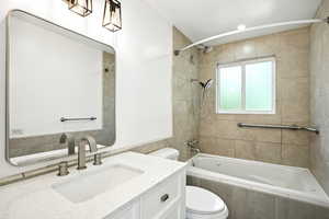 Full bathroom with tiled shower / bath combo, toilet, vanity, and tile walls