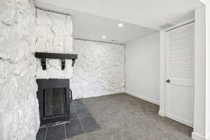 Unfurnished living room featuring dark colored carpet and a stone fireplace