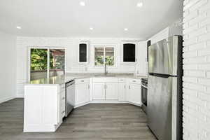 Kitchen featuring appliances with stainless steel finishes, sink, wood-type flooring, and light stone countertops