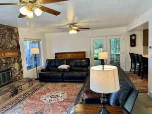 Carpeted living room adjoining kitchen, featuring a textured ceiling, ceiling fan, and a stone fireplace