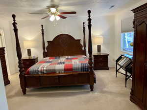 Owner's Suite Bedroom featuring windows with views of wooded lot, french doors out to adjoining large covered deck, ceiling fan, adjoining bathroom, a textured ceiling, and light carpet