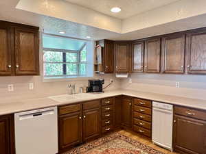 Kitchen with light laminate flooring, sink with a window and view, white dishwasher, and a textured ceiling