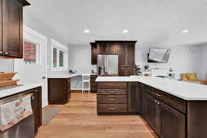 Kitchen featuring light wood-type flooring, dark brown cabinets, stainless steel refrigerator with ice dispenser, a textured ceiling, and refrigerator