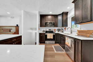 Kitchen featuring light hardwood / wood-style floors, sink, stainless steel appliances, a textured ceiling, and dark brown cabinets