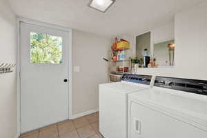 Laundry room featuring washer and dryer, a textured ceiling, electric panel, and light tile patterned floors