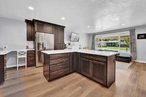 Kitchen with stainless steel fridge, light hardwood / wood-style flooring, dark brown cabinets, and a textured ceiling