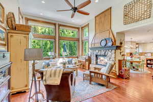 Living room featuring a fireplace, ceiling fan with notable chandelier, a high ceiling, and hardwood / wood-style flooring