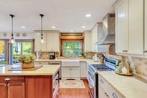 Kitchen featuring a wealth of natural light, sink, appliances with stainless steel finishes, pendant lighting, and wall chimney range hood