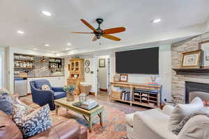 Living room with a fireplace, indoor bar, ceiling fan, and light wood-type flooring