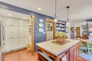 Kitchen featuring white cabinetry, stainless steel refrigerator, light wood-type flooring, wooden walls, and pendant lighting