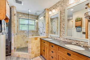 Bathroom featuring dual bowl vanity, decorative backsplash, and a shower with door