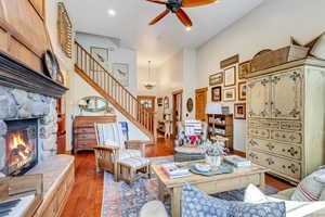 Living room with ceiling fan with notable chandelier, a stone fireplace, wood-type flooring, and a high ceiling