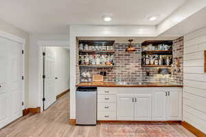 Bar with light hardwood / wood-style flooring, white cabinetry, sink, fridge, and butcher block countertops