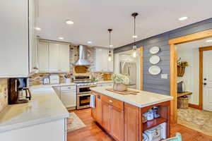 Kitchen featuring wall chimney range hood, stainless steel refrigerator, double oven range, and backsplash