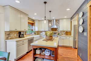 Kitchen with appliances with stainless steel finishes, light hardwood / wood-style flooring, decorative backsplash, and wall chimney exhaust hood