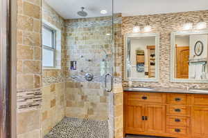 Bathroom with tasteful backsplash, walk in shower, and dual bowl vanity