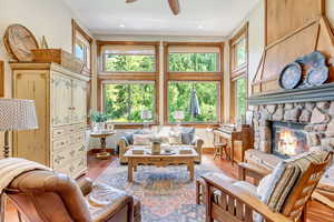 Living room featuring a wealth of natural light, ceiling fan, a stone fireplace, and wood-type flooring