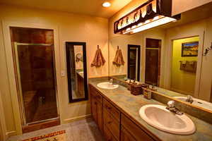 Primary bathroom featuring a tile shower with door and double sink vanity and custom lighting fixure