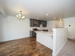 Kitchen with appliances with stainless steel finishes, an inviting chandelier, pendant lighting, a kitchen breakfast bar, and dark carpet