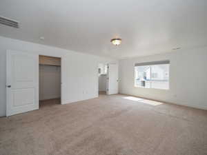 Unfurnished bedroom featuring a spacious closet, light carpet, and a closet