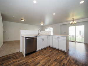 Kitchen with decorative light fixtures, stainless steel dishwasher, sink, kitchen peninsula, and dark carpet