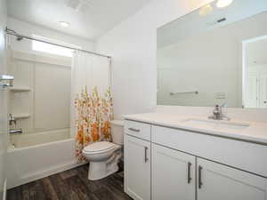 Full bathroom with hardwood / wood-style flooring, vanity, shower / tub combo with curtain, and toilet