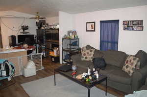 Living room with a textured ceiling, ceiling fan, and dark wood-type flooring