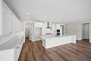 Kitchen with gas cooktop, wall chimney exhaust hood, dark wood-type flooring, a spacious island, and white cabinets