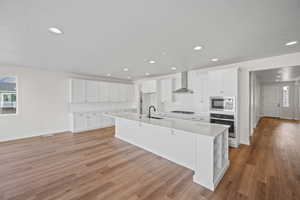 Kitchen with sink, wall chimney exhaust hood, stainless steel appliances, a large island with sink, and light wood-type flooring