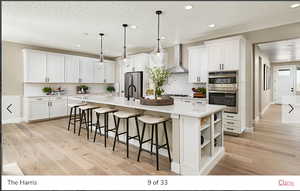 Kitchen featuring appliances with stainless steel finishes, light hardwood / wood-style floors, wall chimney exhaust hood, tasteful backsplash, and a center island with sink