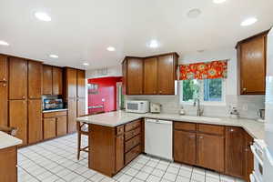 Kitchen with backsplash, light tile patterned floors, sink, kitchen peninsula, and white appliances