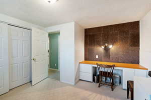 Carpeted office space featuring a textured ceiling and built in desk