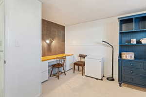 Home office featuring light colored carpet, a textured ceiling, and built in desk