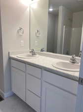 Primary bath with double sinks, white shaker cabinets,  and laminate counters.