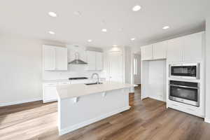 Kitchen featuring a kitchen island with sink, oven, sink, built in microwave, and white cabinetry