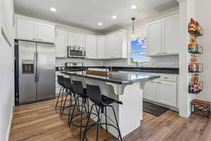 Kitchen with a center island, light hardwood / wood-style floors, white cabinetry, stainless steel appliances, and pendant lighting