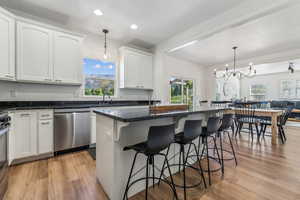 Kitchen with stainless steel appliances, light hardwood / wood-style floors, pendant lighting, white cabinets, and a kitchen island