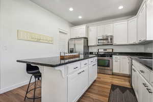 Kitchen with appliances with stainless steel finishes, white cabinetry, and dark hardwood / wood-style floors