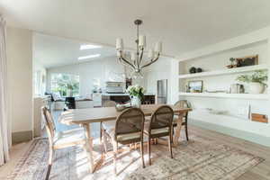 Dining area with built in features, a chandelier, lofted ceiling with skylight, and light hardwood / wood-style floors