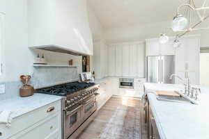 Kitchen with light stone countertops, hanging light fixtures, premium appliances, and white cabinetry