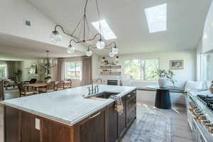 Kitchen with a skylight, hanging light fixtures, light wood-type flooring, a kitchen island with sink, and double oven range