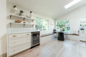 Bar with plenty of natural light, beverage cooler, light hardwood / wood-style flooring, and lofted ceiling with skylight