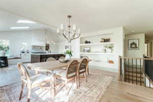 Dining space featuring built in shelves, a chandelier, light hardwood / wood-style floors, and lofted ceiling with skylight