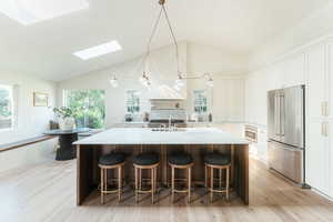 Kitchen with vaulted ceiling with skylight, plenty of natural light, stainless steel appliances, and a center island with sink