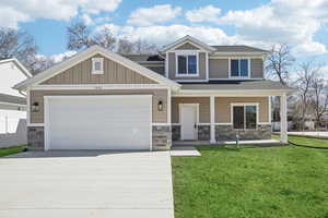 Craftsman-style house featuring a porch, board and batten siding, a garage, driveway, and stone.Grass is not included. Added for visualization.