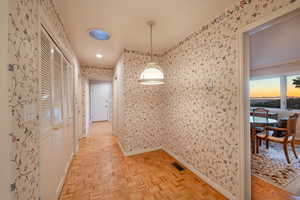 Hallway with light parquet flooring leading from kitchen to sunroom